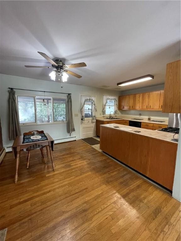 kitchen with a baseboard radiator, light wood-style flooring, a peninsula, light countertops, and a sink