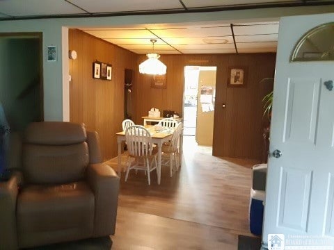 dining space with a drop ceiling, wooden walls, and hardwood / wood-style flooring