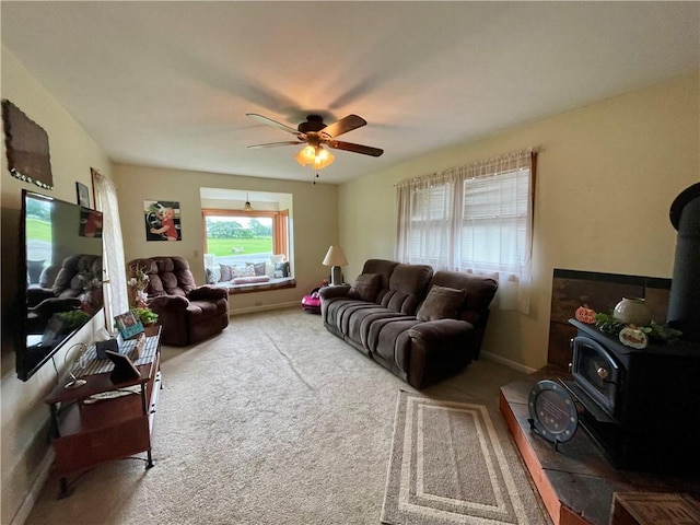 carpeted living room featuring a wood stove and ceiling fan