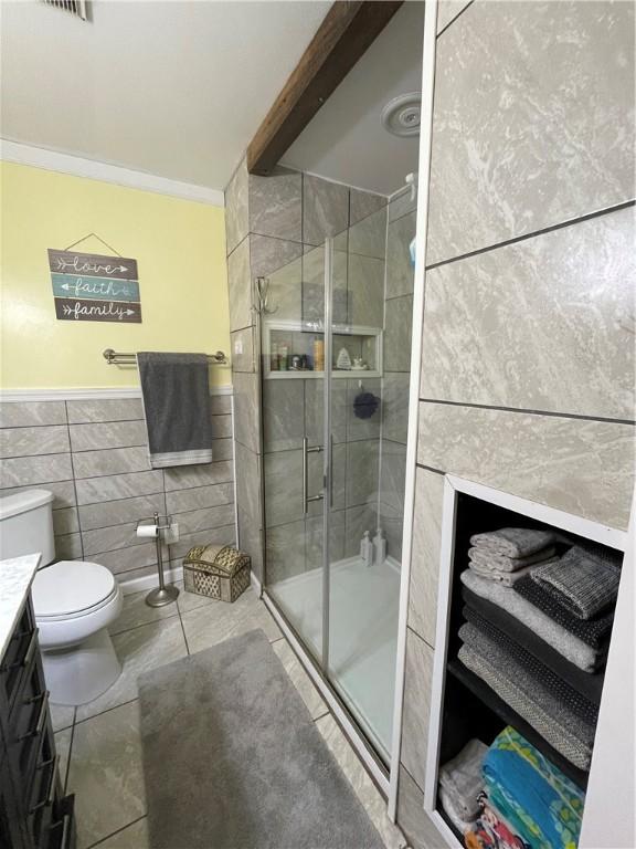 bathroom with tile patterned floors, toilet, vanity, tile walls, and an enclosed shower