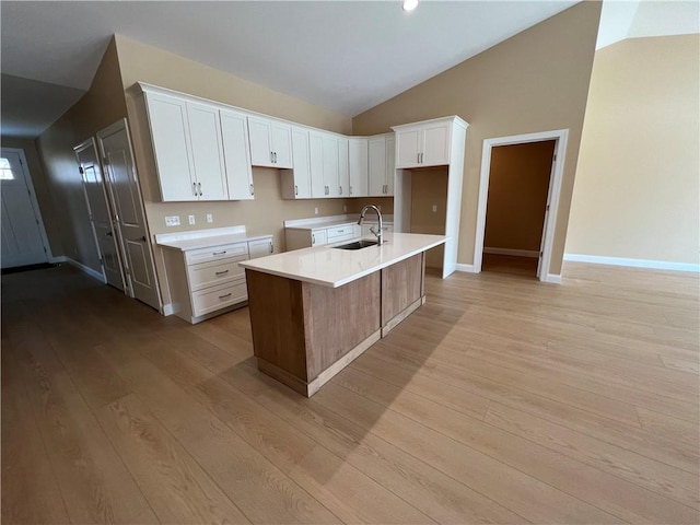 kitchen with a sink, light wood-style floors, vaulted ceiling, and white cabinetry