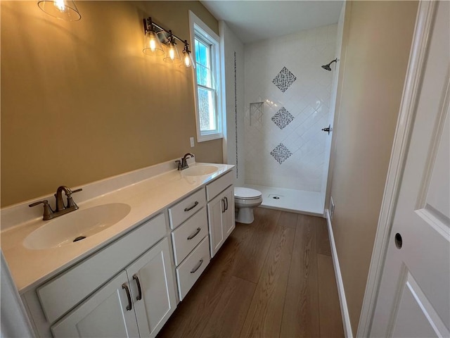 full bath featuring a sink, toilet, wood finished floors, and a tile shower