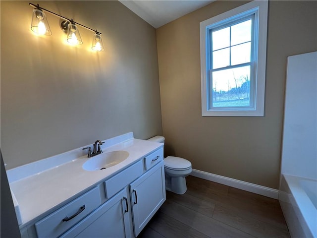 full bath featuring toilet, wood finished floors, baseboards, a bathtub, and vanity