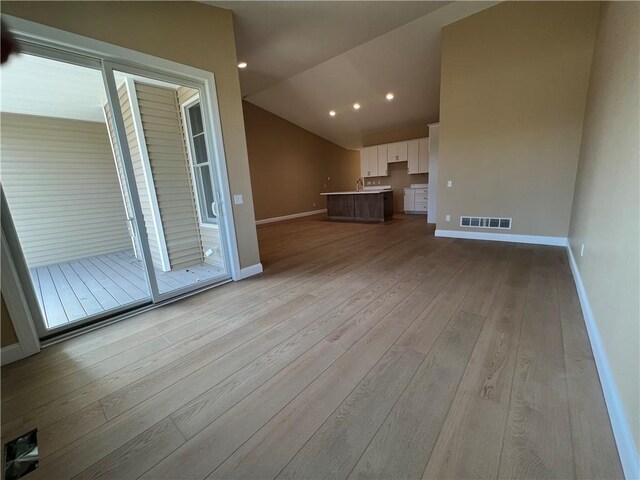 unfurnished living room featuring lofted ceiling, wood finished floors, visible vents, and baseboards