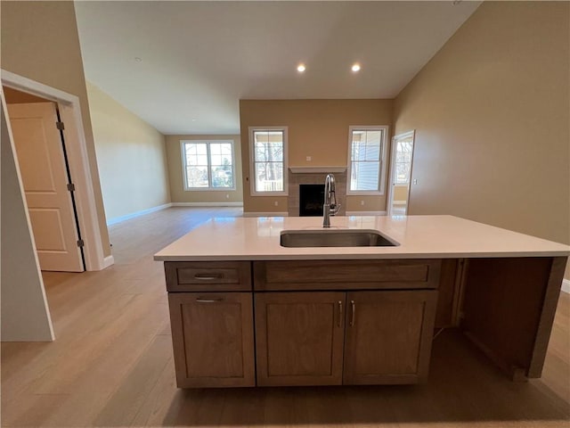 kitchen with light wood-style flooring, a sink, open floor plan, light countertops, and a tile fireplace