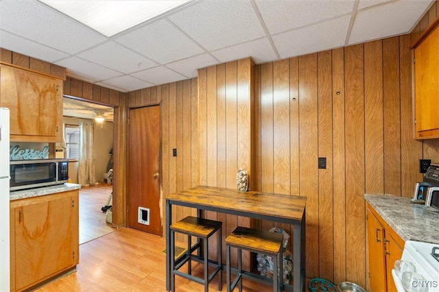 kitchen with wood walls, light hardwood / wood-style flooring, stove, and a paneled ceiling