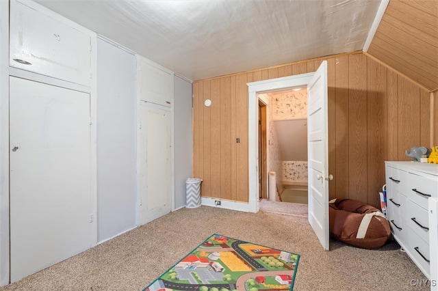 carpeted bedroom with vaulted ceiling and wood walls