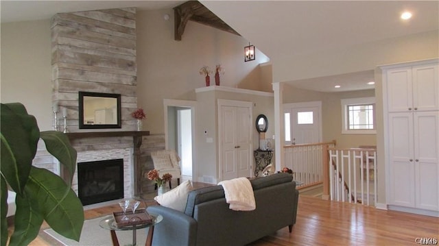 living room with light hardwood / wood-style floors, high vaulted ceiling, and a stone fireplace