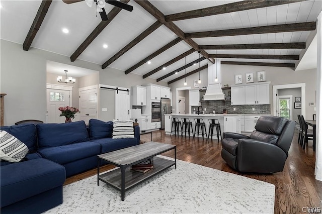 living room with ceiling fan with notable chandelier, dark hardwood / wood-style flooring, sink, lofted ceiling with beams, and a barn door