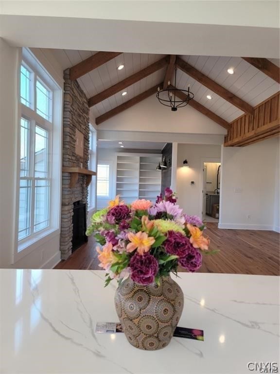 interior space with wooden ceiling, a stone fireplace, wood-type flooring, and vaulted ceiling with beams