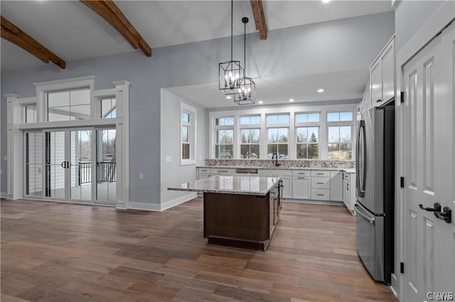 kitchen featuring hardwood / wood-style floors, stainless steel refrigerator, white cabinetry, a kitchen island, and light stone countertops