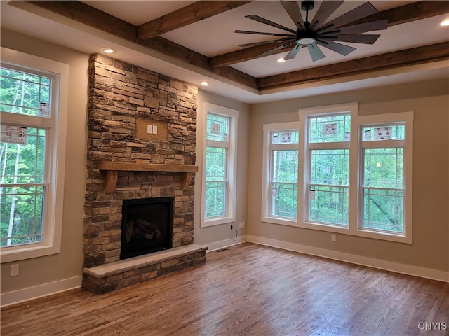 unfurnished living room featuring a wealth of natural light, hardwood / wood-style floors, ceiling fan, and a stone fireplace