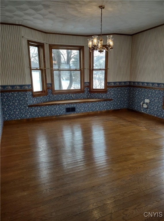 empty room featuring crown molding, a chandelier, and hardwood / wood-style floors