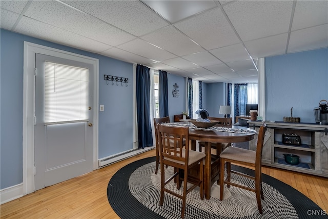 dining space featuring a paneled ceiling, light hardwood / wood-style floors, and baseboard heating