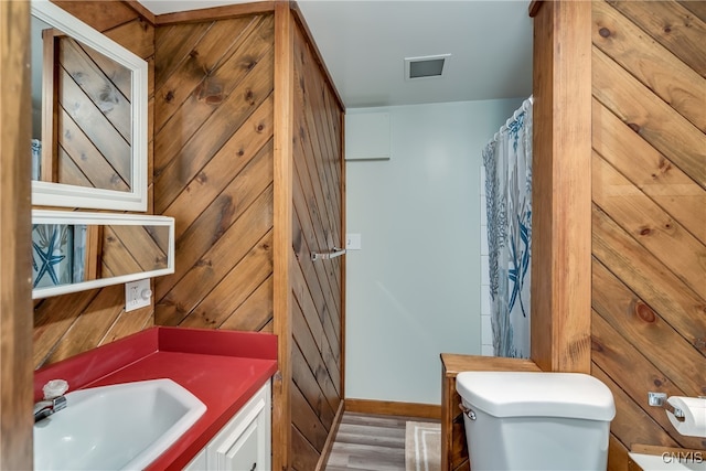 bathroom with wooden walls, vanity, hardwood / wood-style floors, and toilet