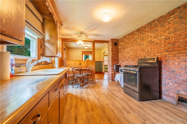 kitchen with light hardwood / wood-style flooring, brick wall, sink, stainless steel gas range, and ceiling fan