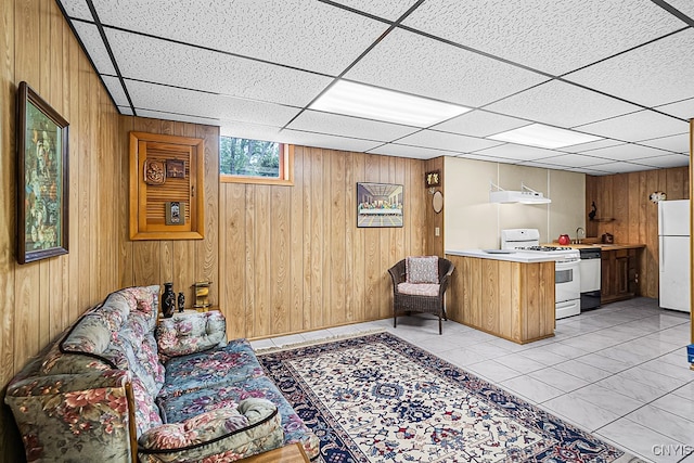 tiled living room featuring a drop ceiling and wood walls