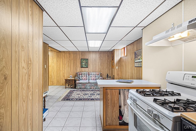 kitchen with light tile patterned floors, range hood, white gas stove, and wood walls