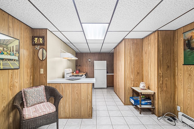 kitchen featuring baseboard heating, wooden walls, light tile patterned flooring, and white appliances