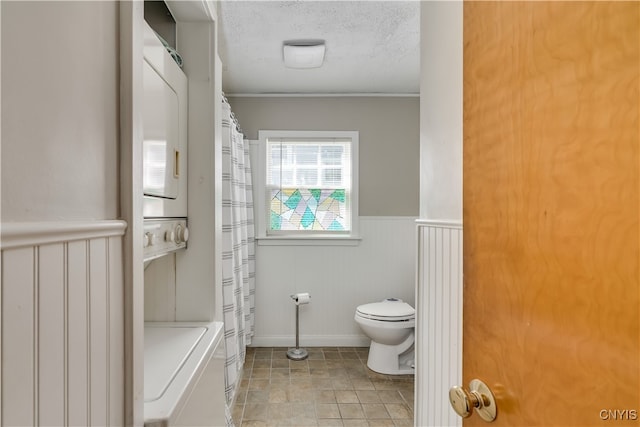 bathroom featuring tile patterned floors, a textured ceiling, stacked washer / drying machine, toilet, and walk in shower