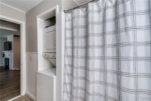 bathroom featuring hardwood / wood-style floors, stacked washing maching and dryer, a fireplace, curtained shower, and crown molding