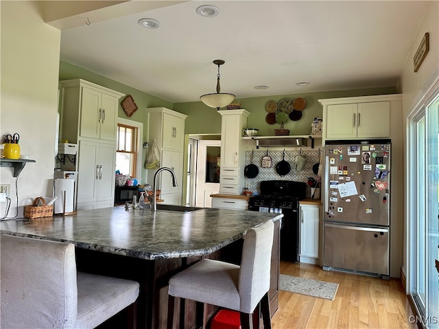 kitchen featuring a breakfast bar, black range, light hardwood / wood-style floors, white cabinetry, and stainless steel fridge