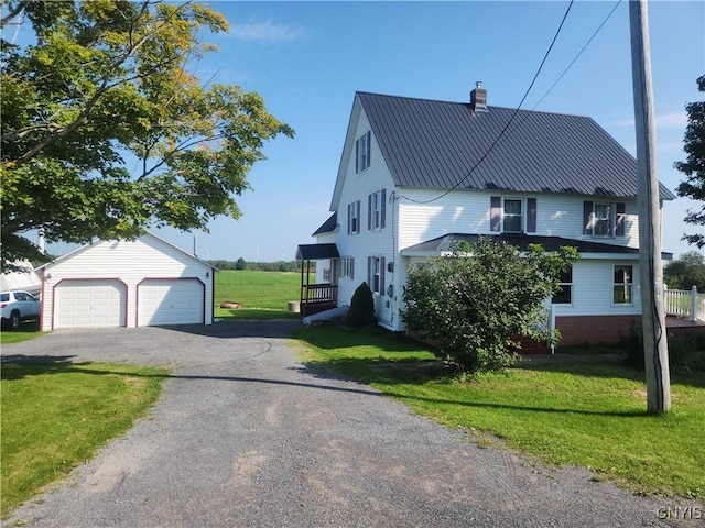 view of front of house with a front yard, a chimney, metal roof, a garage, and an outbuilding