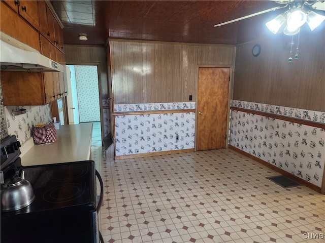 kitchen with ceiling fan, wood walls, and stove