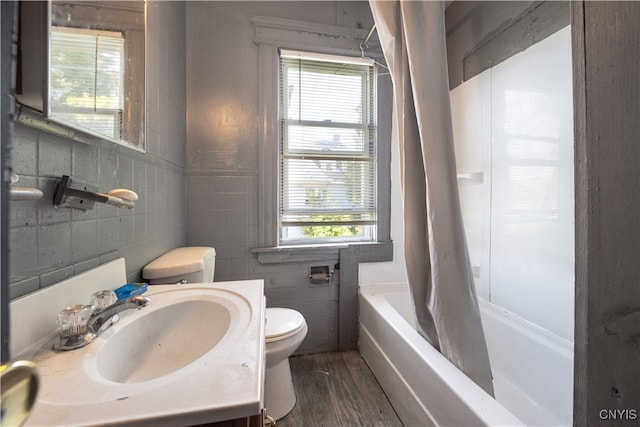 full bathroom with hardwood / wood-style floors, toilet, vanity, tile walls, and shower / tub combo