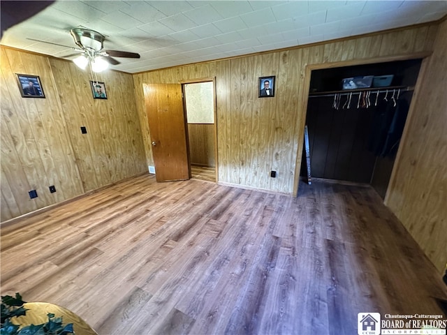 empty room with ceiling fan, hardwood / wood-style flooring, and wooden walls