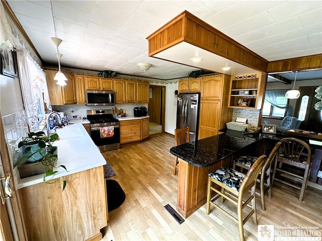 kitchen featuring appliances with stainless steel finishes, light wood-type flooring, a kitchen bar, and hanging light fixtures