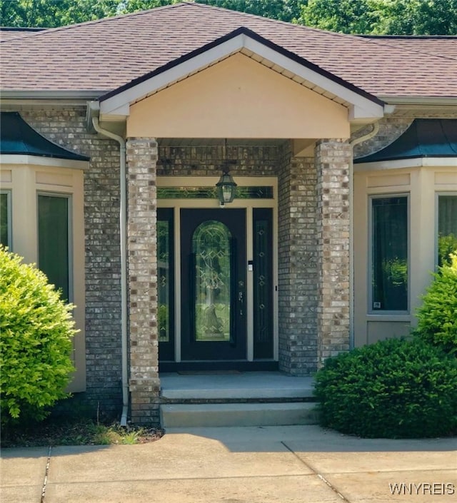 doorway to property featuring stone siding, brick siding, and a shingled roof