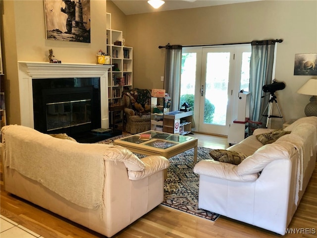 living area with a fireplace with flush hearth, wood finished floors, and french doors