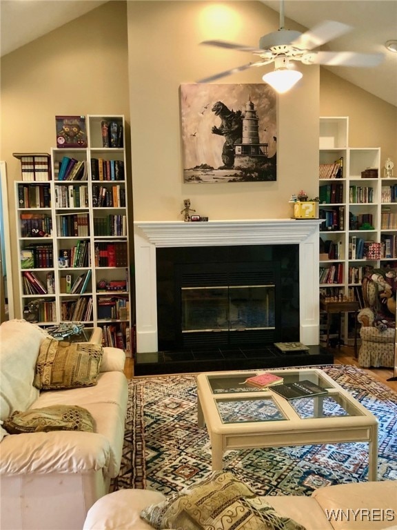 living area with lofted ceiling, a fireplace with flush hearth, a ceiling fan, and wood finished floors