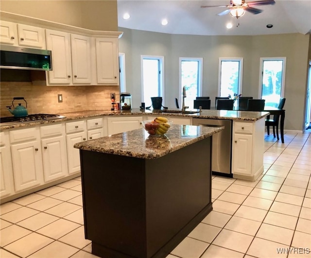 kitchen featuring light tile patterned floors, stainless steel appliances, a peninsula, backsplash, and a center island