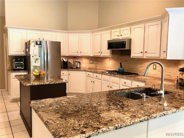 kitchen featuring light tile patterned flooring, a sink, appliances with stainless steel finishes, backsplash, and dark stone countertops