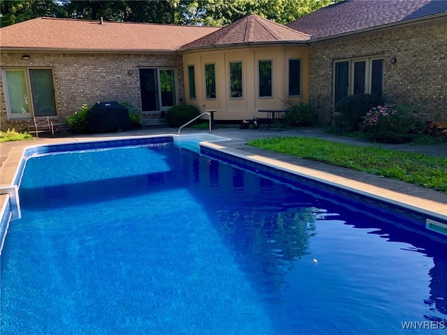 outdoor pool with entry steps, a patio, and area for grilling