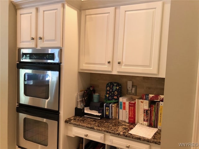 kitchen with double oven, dark stone counters, and white cabinetry