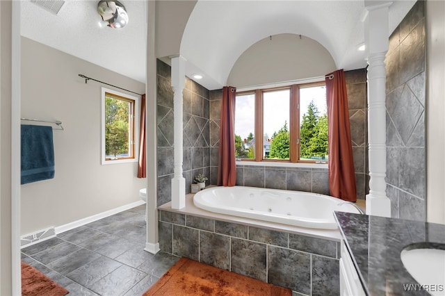 bathroom with a wealth of natural light, vanity, a relaxing tiled tub, and toilet