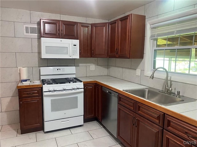 kitchen featuring white appliances, a sink, visible vents, tile counters, and tasteful backsplash