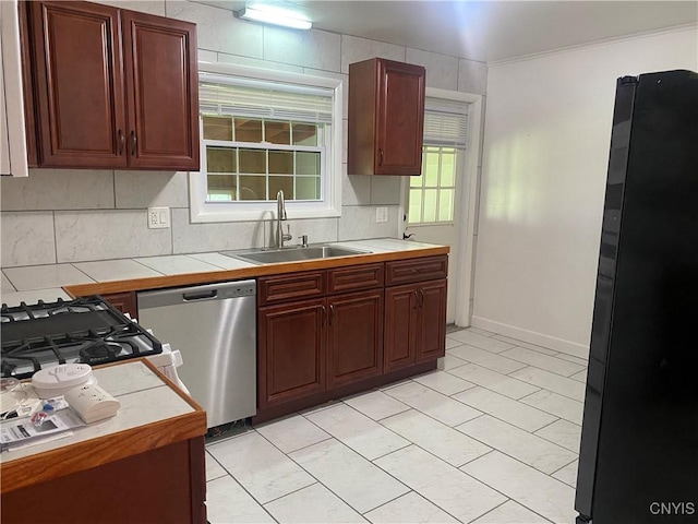 kitchen featuring tile counters, dishwasher, backsplash, freestanding refrigerator, and a sink