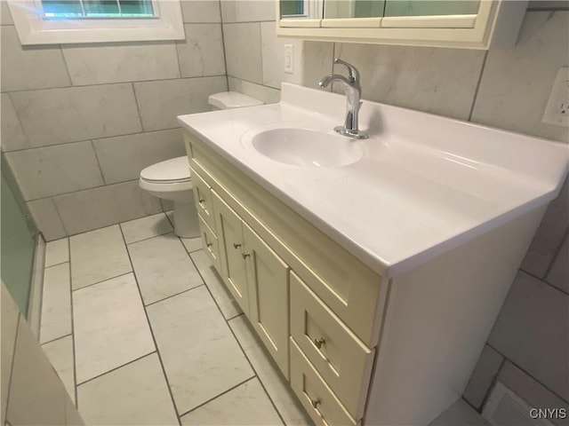 bathroom with marble finish floor, vanity, toilet, and tile walls