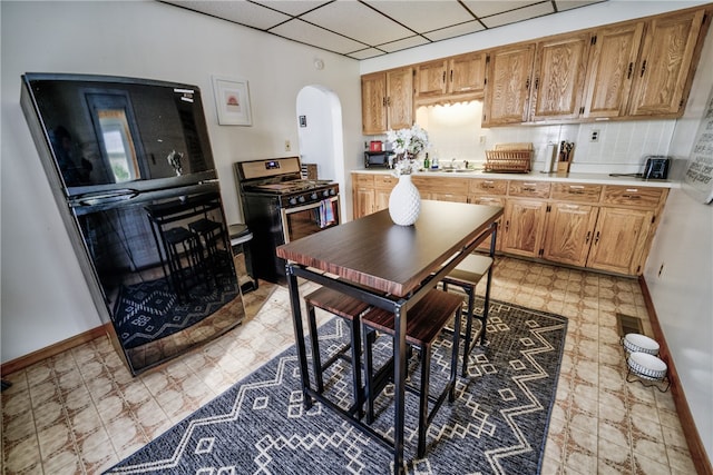 kitchen featuring sink, stainless steel gas stove, light tile patterned flooring, and a drop ceiling