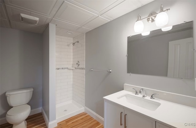 bathroom with toilet, hardwood / wood-style flooring, a tile shower, and vanity