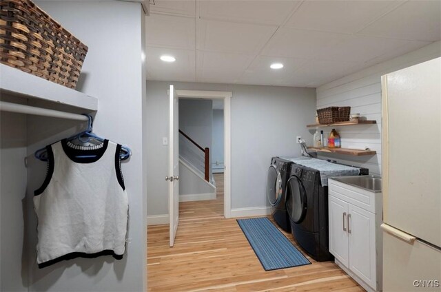 clothes washing area featuring light wood-type flooring, washing machine and clothes dryer, and cabinets