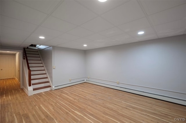 basement with a baseboard heating unit, wood-type flooring, and a drop ceiling