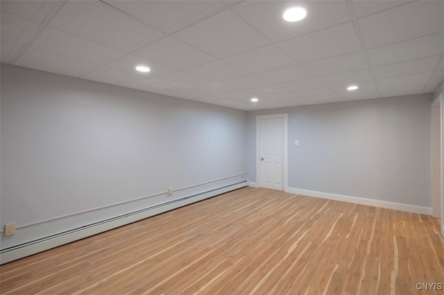 empty room featuring baseboard heating, wood-type flooring, and a drop ceiling