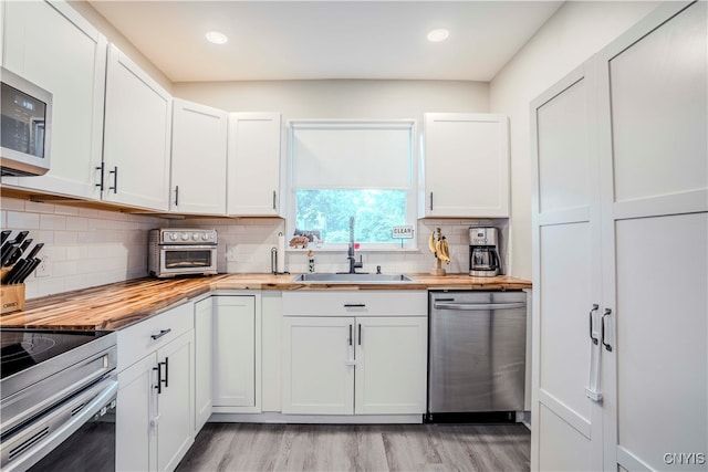 kitchen with butcher block countertops, appliances with stainless steel finishes, tasteful backsplash, light hardwood / wood-style floors, and white cabinets