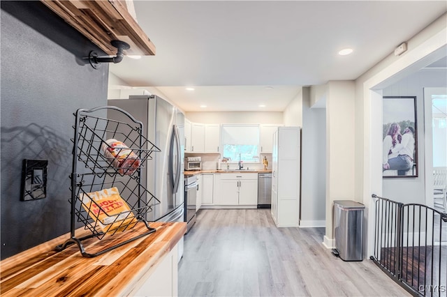 kitchen with appliances with stainless steel finishes, decorative backsplash, white cabinetry, butcher block counters, and light wood-type flooring