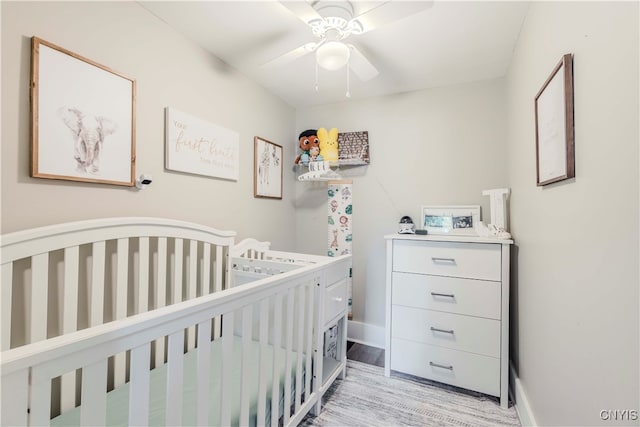 bedroom featuring light hardwood / wood-style flooring, ceiling fan, and a crib